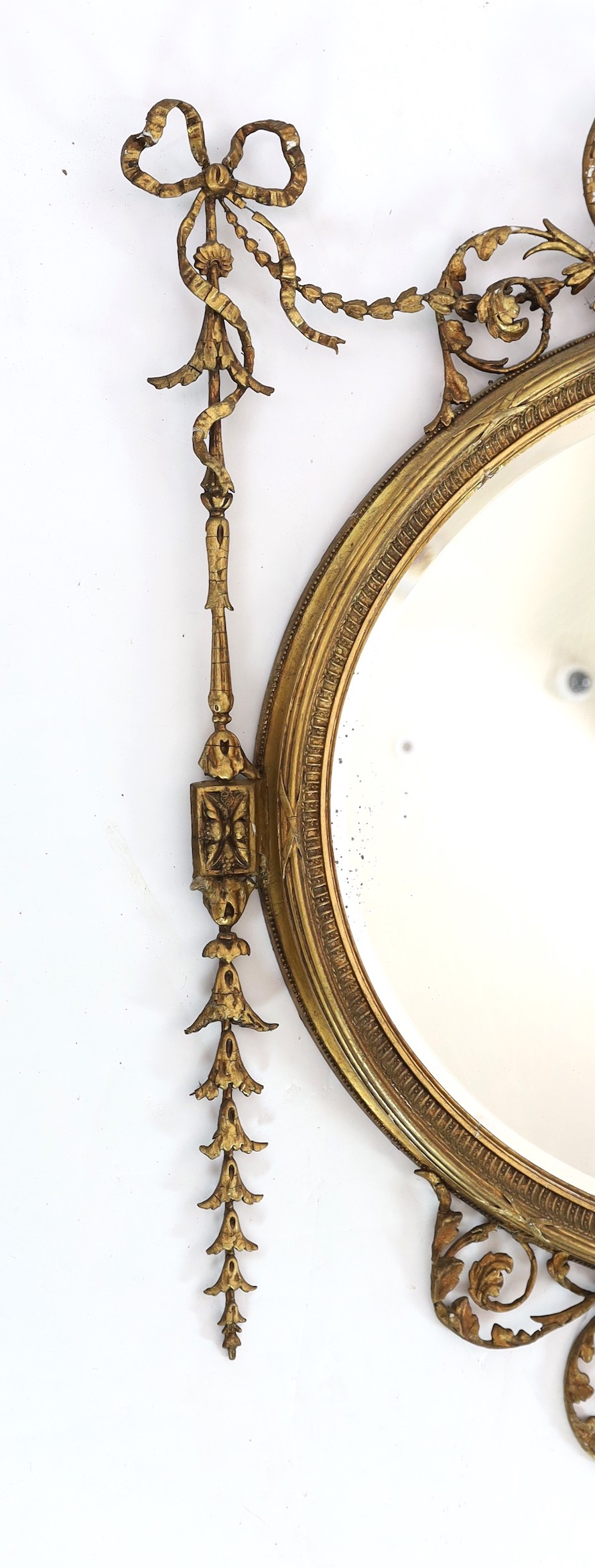 A late Victorian Adam Revival oval wall mirror, with urn, foliate scroll, ribbon and harebell motifs, and bevelled glass plate, width 119cm, height 118cm